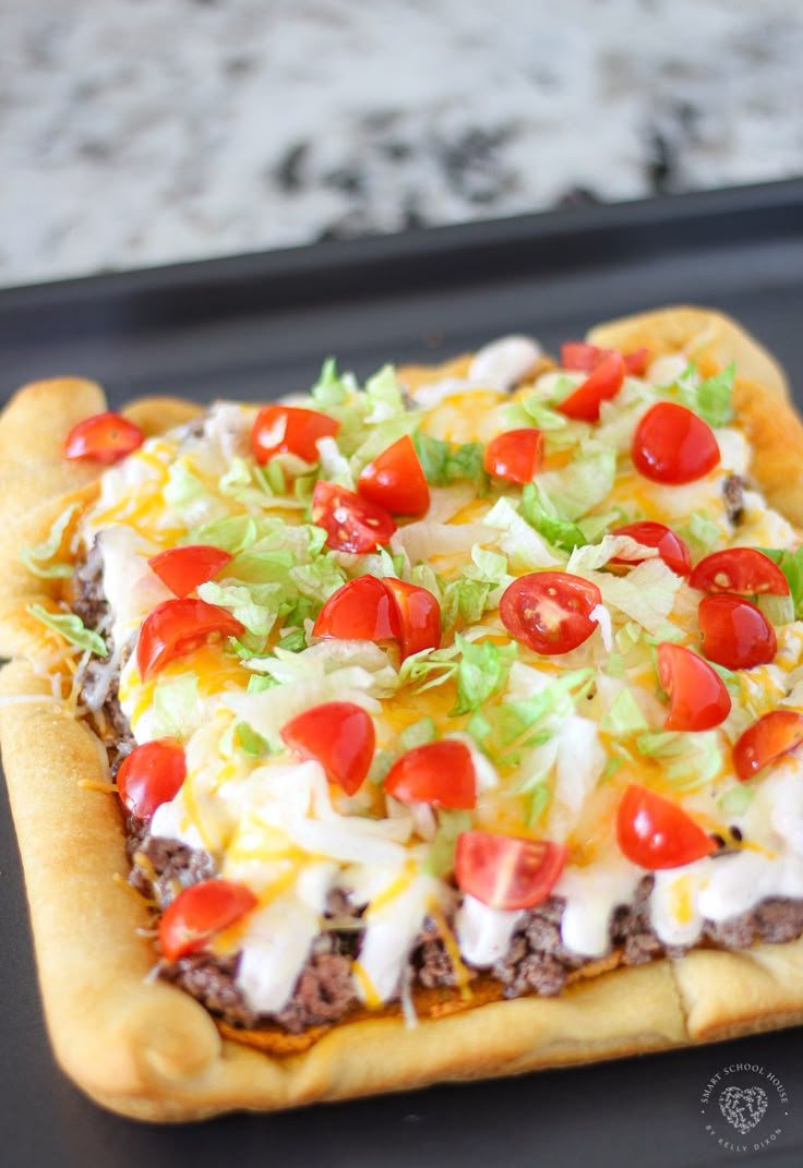 a square pizza topped with cheese, tomatoes and lettuce on a baking sheet