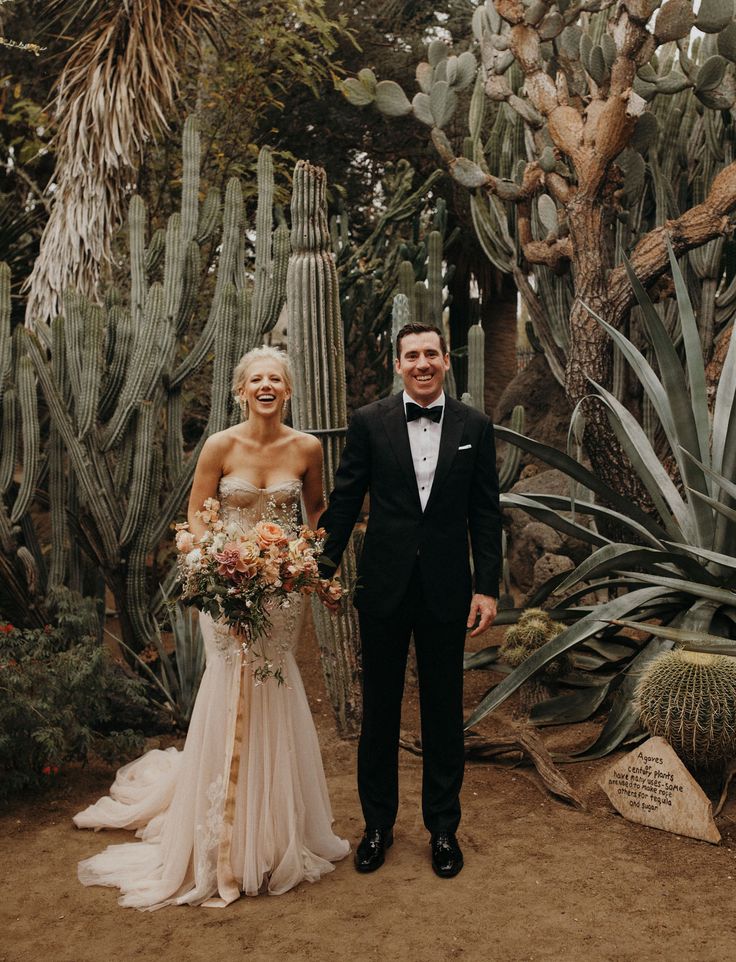 a man and woman standing next to each other in front of cacti