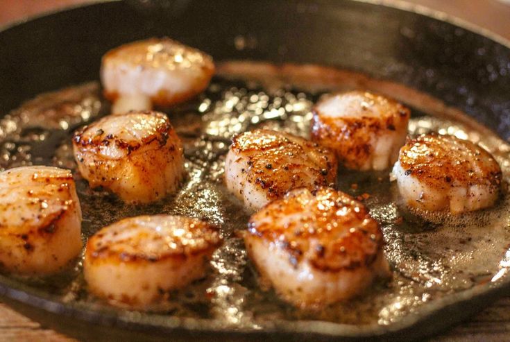 seared scallops cooking in a skillet on top of a wooden table