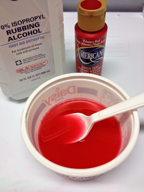 a bowl of red liquid next to a bottle of mouthwash and a plastic spoon