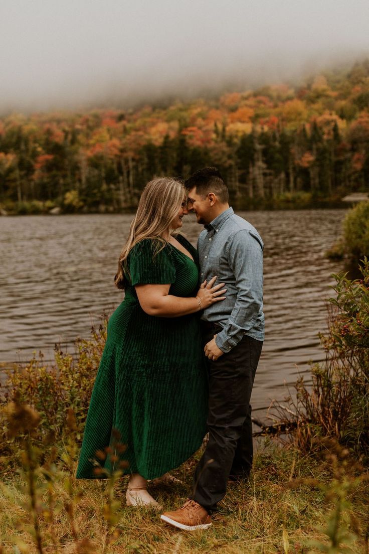 a man and woman standing next to each other in front of a lake