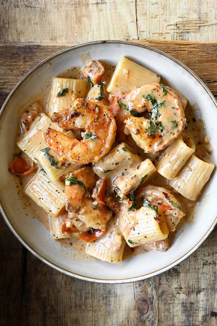 a white bowl filled with pasta and shrimp covered in sauce on top of a wooden table