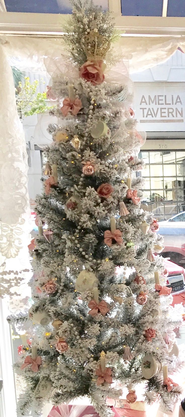 a white christmas tree is decorated with pink and gold ornaments, ribbons and bows in front of a window