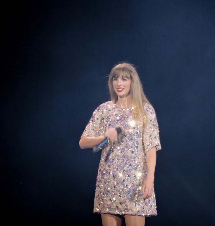 a woman standing in front of a microphone on stage wearing a sequined dress