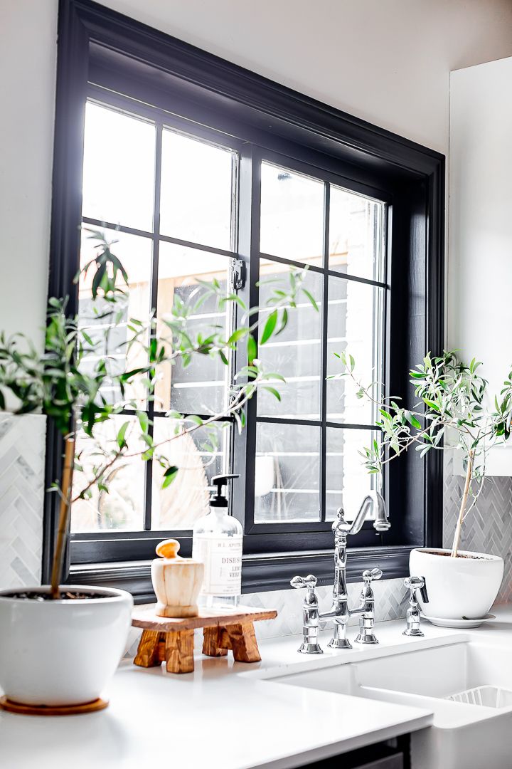 a kitchen with white counter tops and black framed windows, plants on the window sill