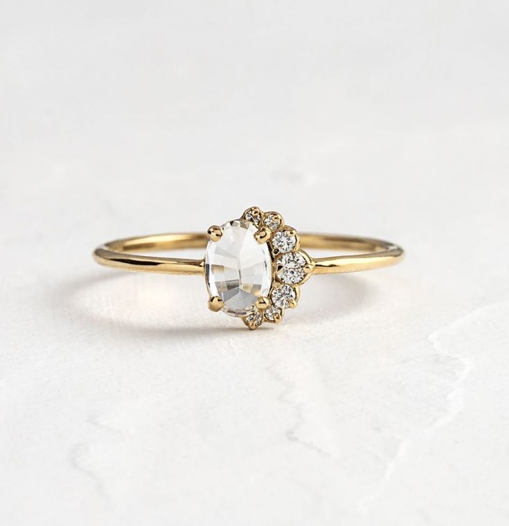 a gold ring with an oval white stone surrounded by small diamonds