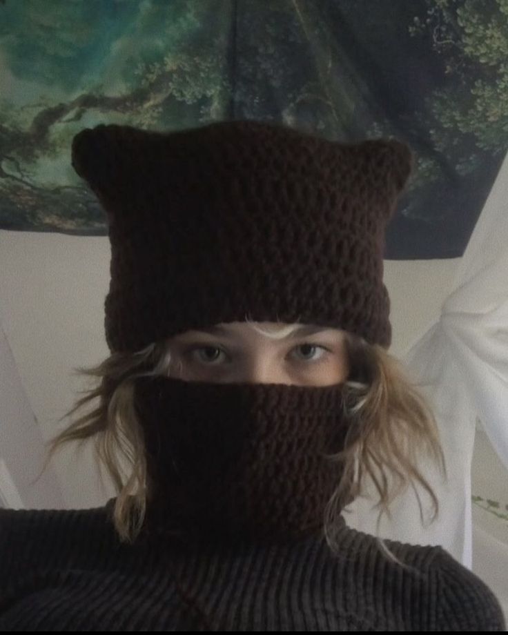 a woman wearing a knitted hat with a bear on it's head and covering her face