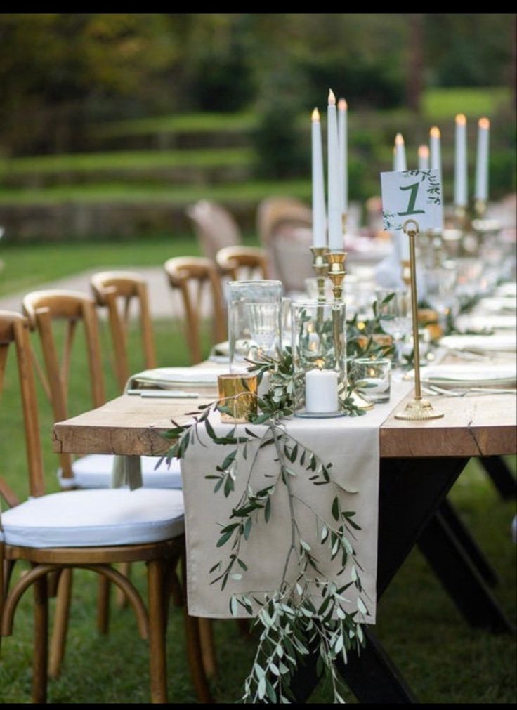 an outdoor table set up with candles and place settings for dinner or wedding guests to sit at