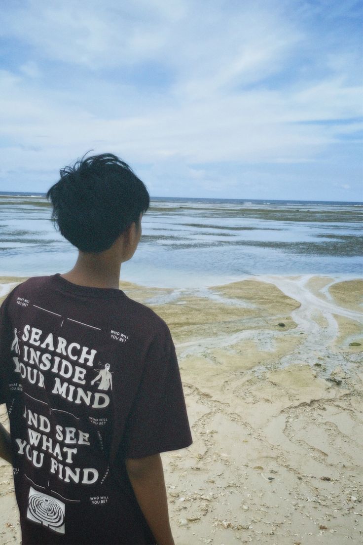 a young man standing on top of a sandy beach next to the ocean and looking at the water