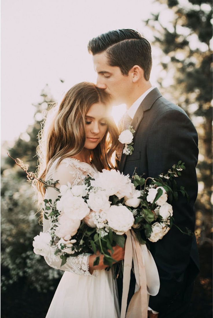 a bride and groom embracing each other in front of some trees with sun shining on them