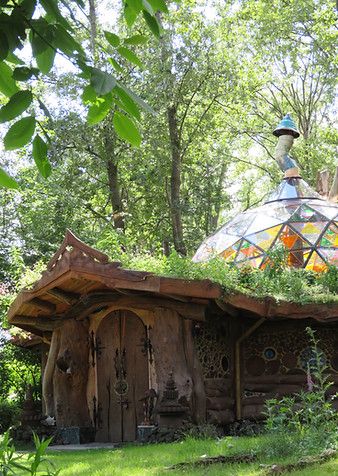 a house made out of wood and glass in the woods with plants growing on top