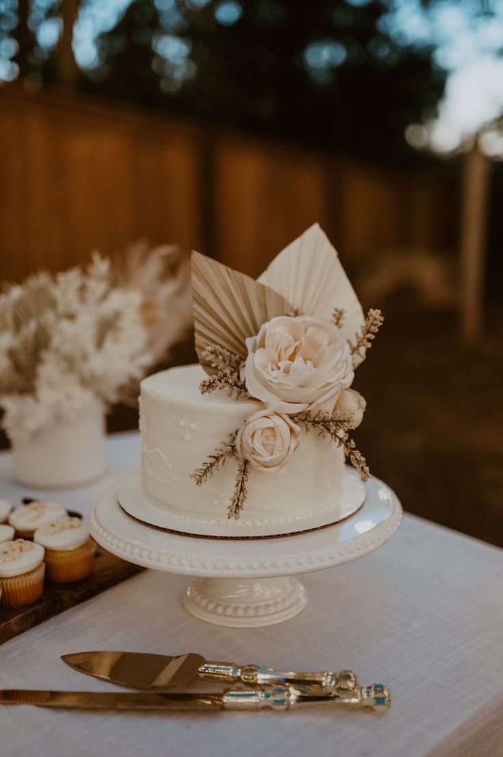 a white cake sitting on top of a table next to cupcakes and silverware