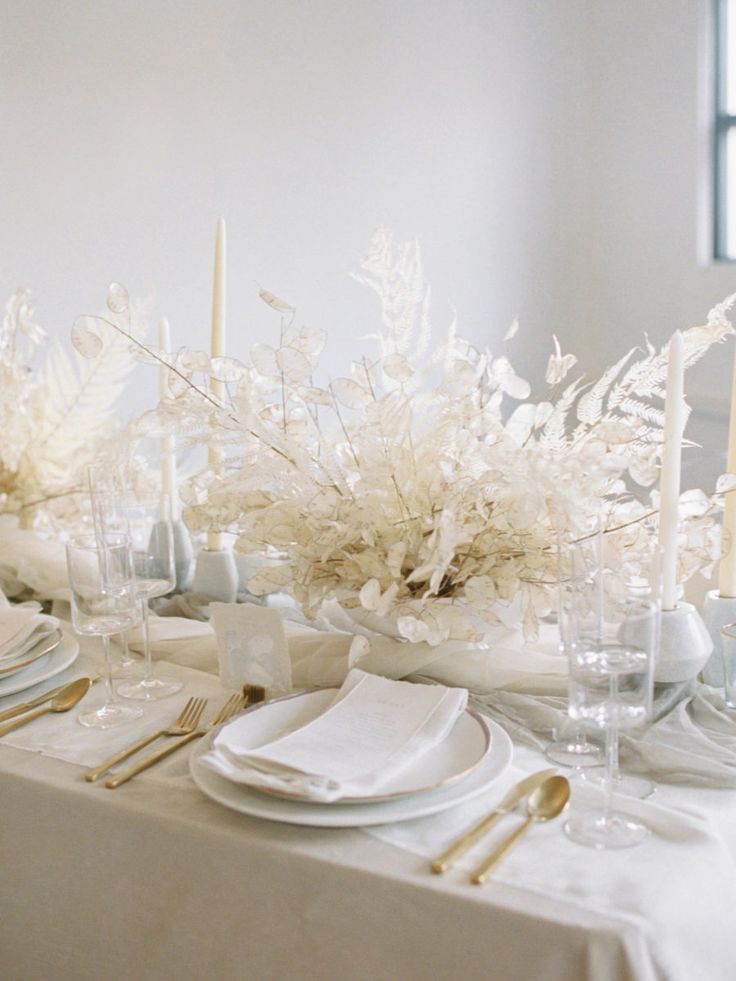 the table is set with white flowers and place settings for an elegant dinner party or special event