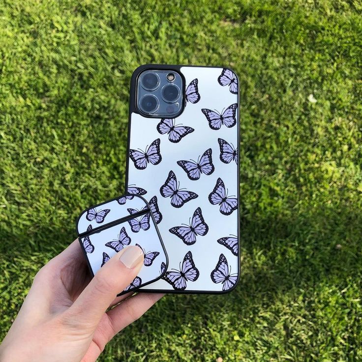 a hand holding an iphone case with butterflies on it in front of some green grass