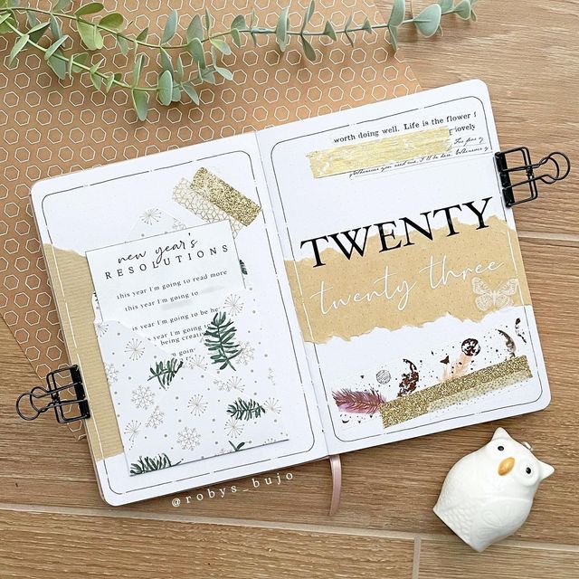 an open planner book sitting on top of a wooden table next to a white vase