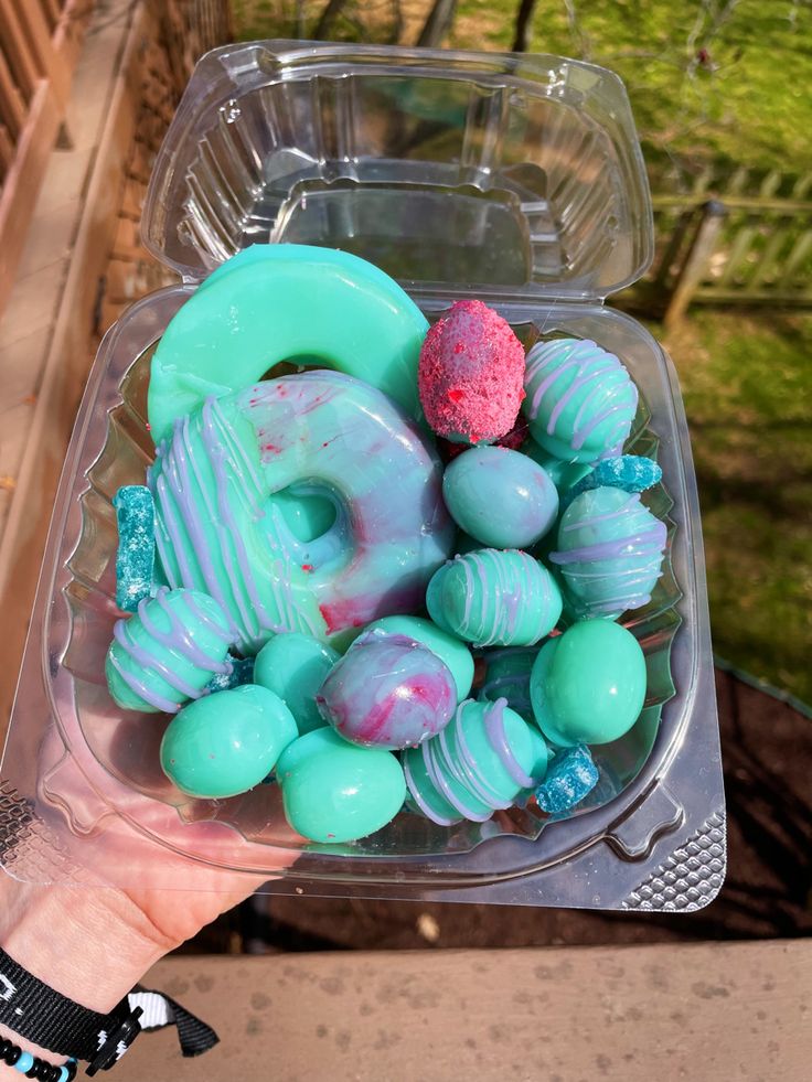 a plastic container filled with candy covered in blue and green frosting next to a hand