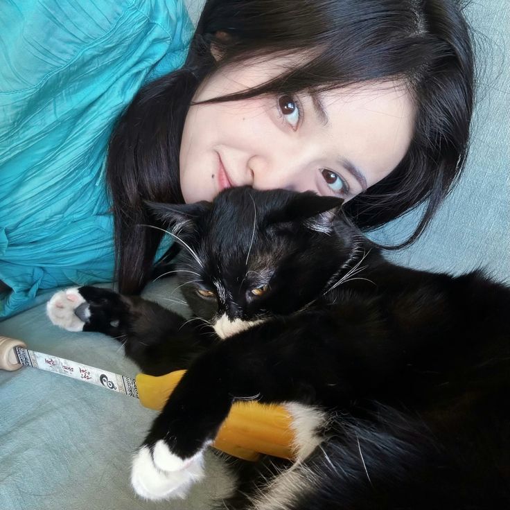 a woman laying on top of a bed holding a black and white cat