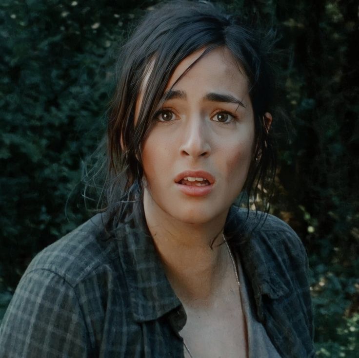 a close up of a person with trees in the background and bushes behind her looking at the camera