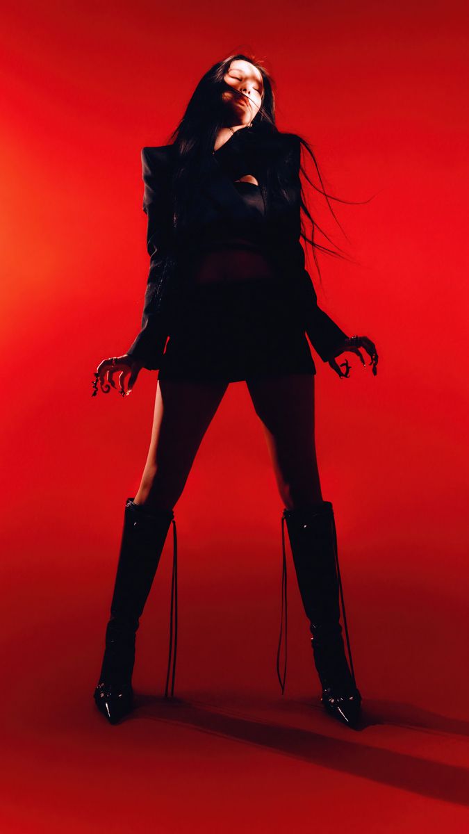 a woman with long hair and black boots posing in front of a red background,