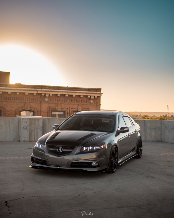 a car parked in an empty parking lot with the sun setting behind it and some buildings