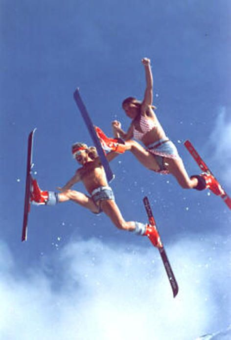 two women are jumping in the air on skis