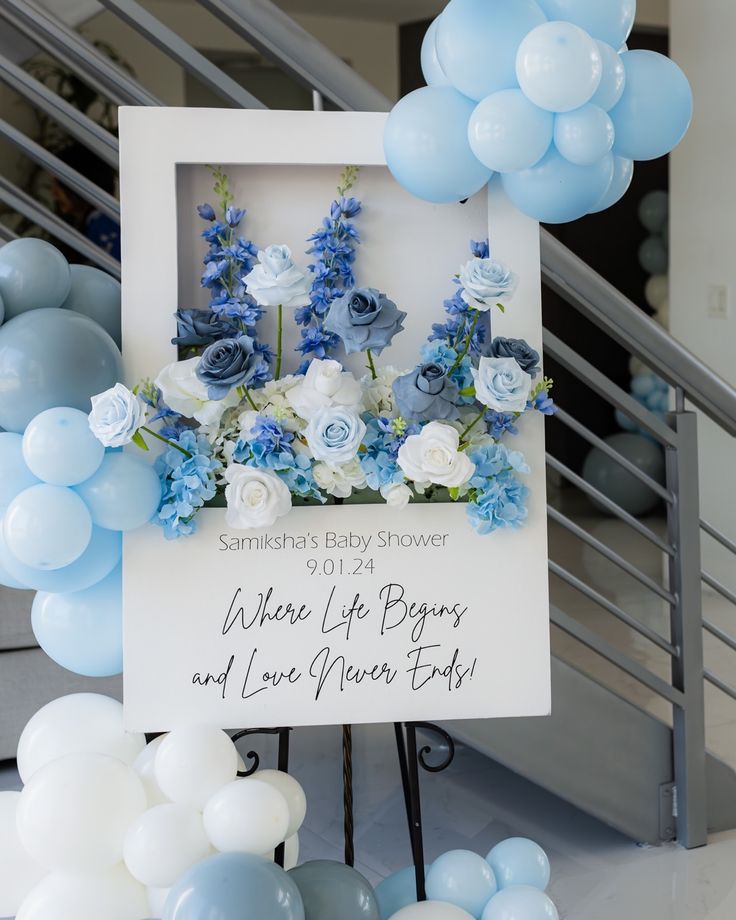 a baby shower sign with blue and white flowers on it next to balloons in the air