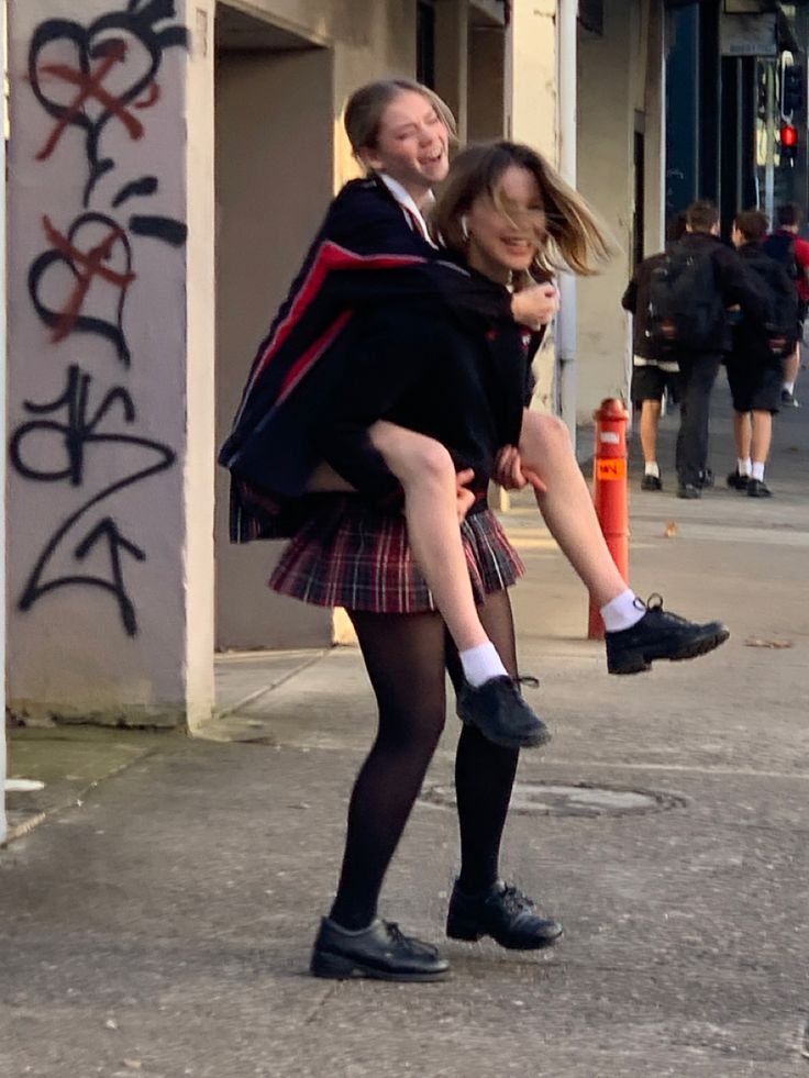 two girls in school uniforms are carrying each other on their shoulders as they walk down the street