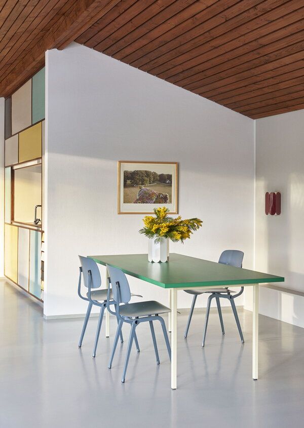 a green table with blue chairs in a white room