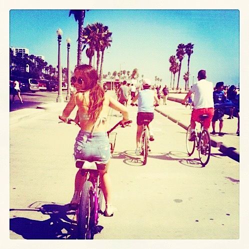 a woman riding a bike down a street next to other people on bikes and palm trees