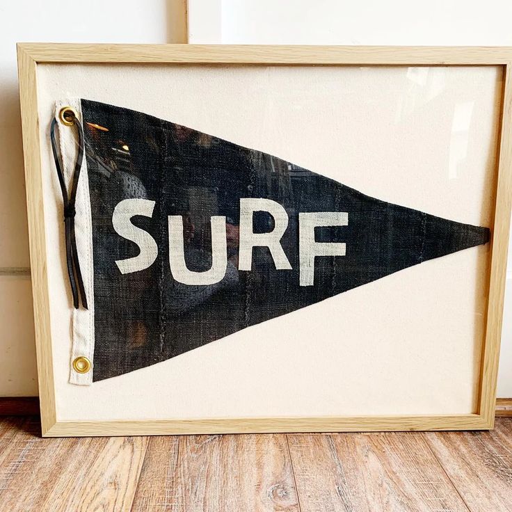 a framed surf sign sitting on top of a wooden floor next to a white wall