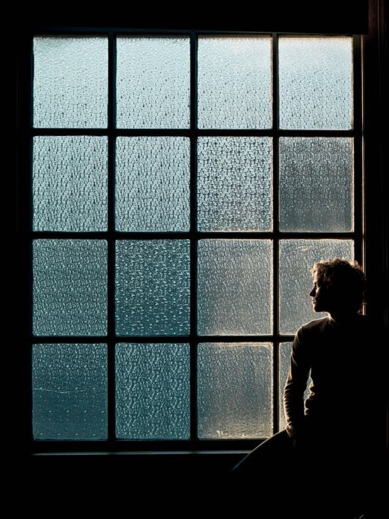 a person sitting in front of a window with rain drops on the glass and looking out