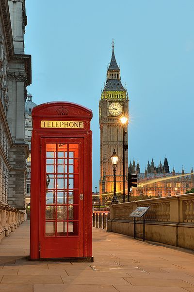 a red phone booth sitting on the side of a road next to a clock tower