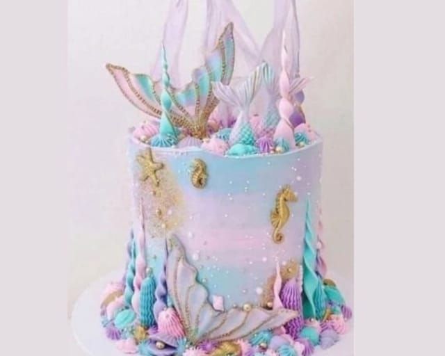 there is a blue and pink cake with mermaid decorations on the top, along with sea shells