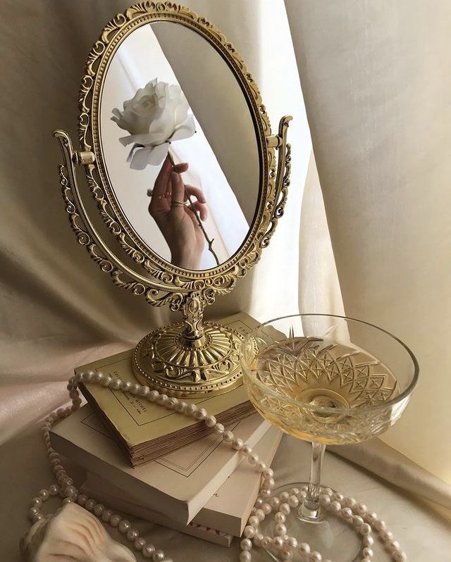 a table topped with a mirror next to a glass filled with liquid and pearls on top of it