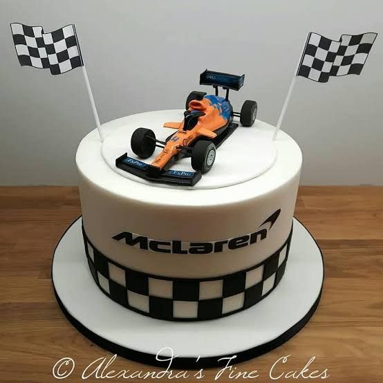 a birthday cake with a racing car on top and checkered flags in the air