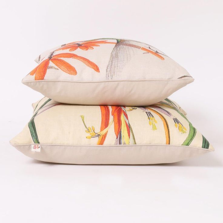 two pillows sitting side by side on top of each other, one with an orange flower