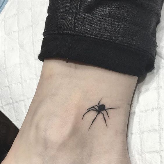 a small black spider tattoo on the left side of the ankle, with an arrow at the bottom