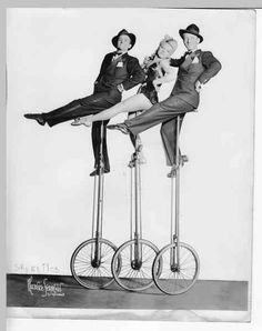 an old photo of three women sitting on top of two unicycles