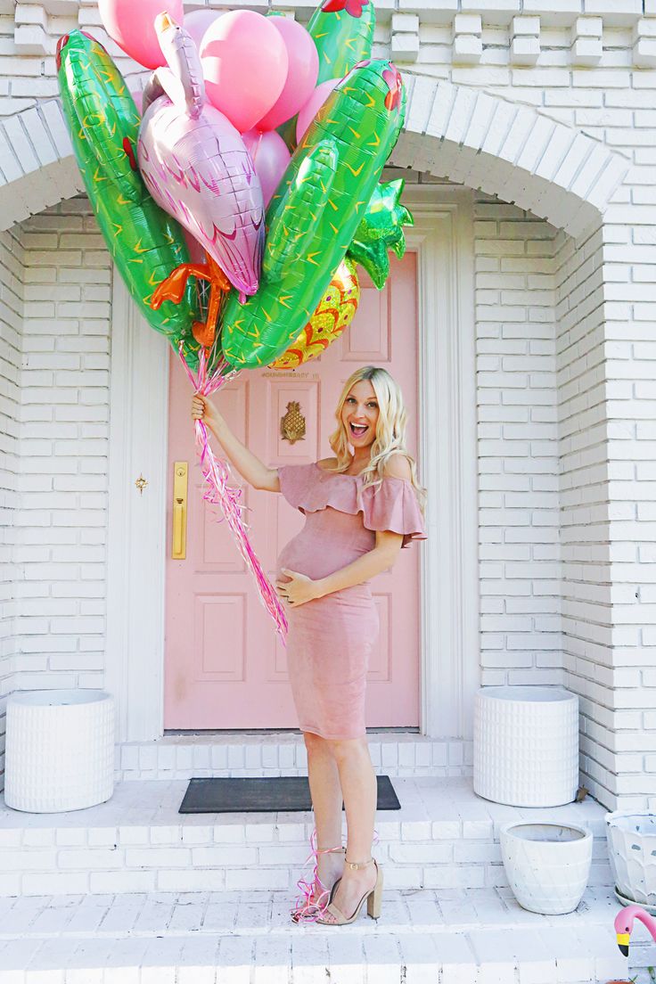 a pregnant woman holding balloons in front of a pink door