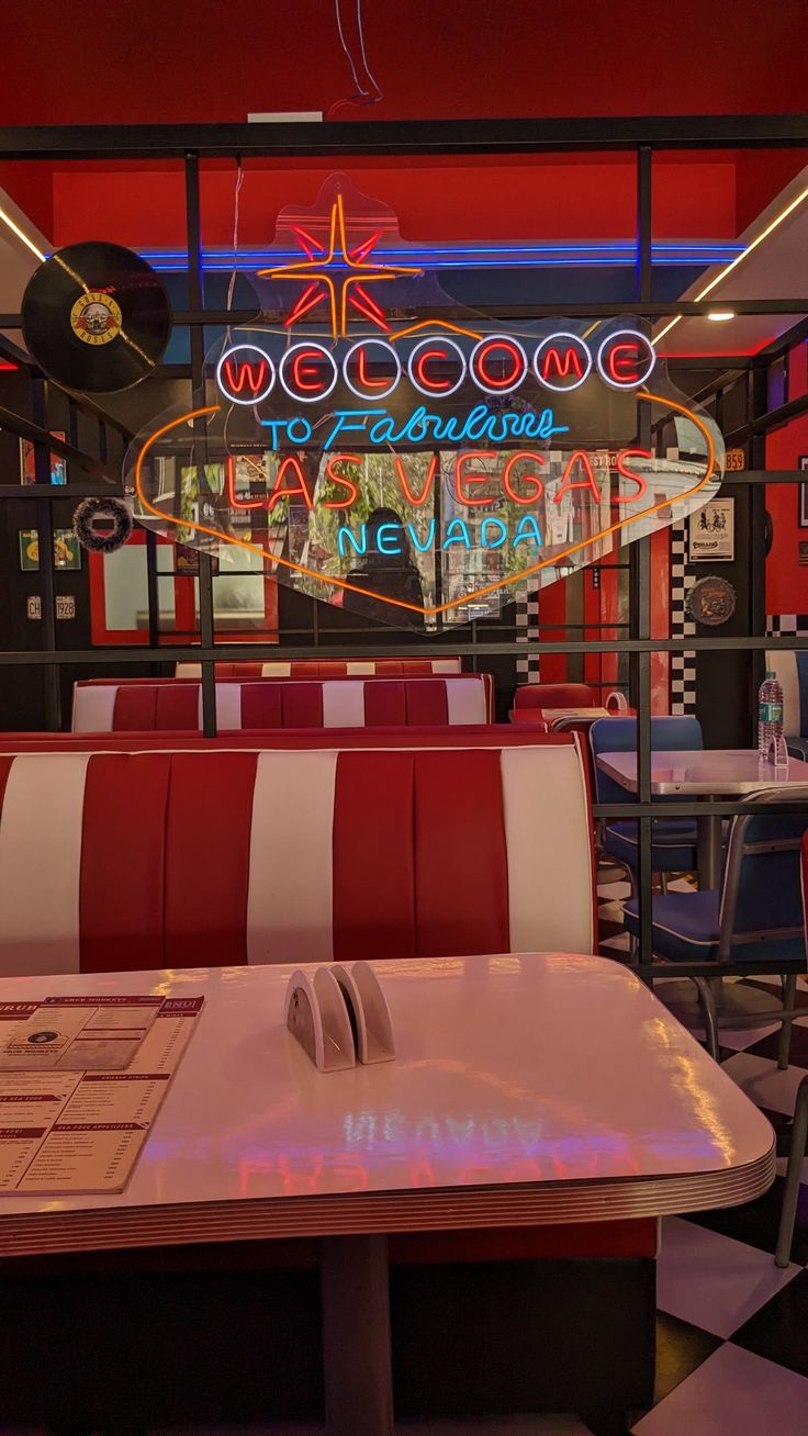 the interior of a diner with neon signs on the walls and tables in front of them