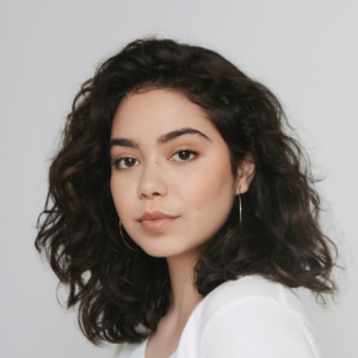 a close up of a person wearing a white shirt and long curly hair with brown eyes