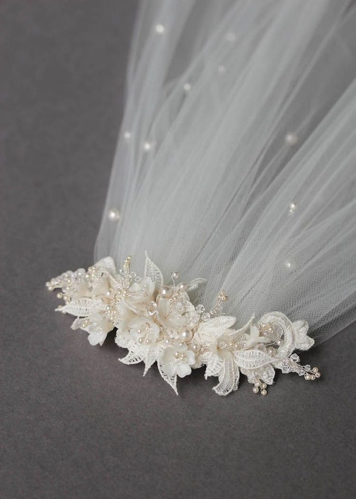 a bridal hair piece with white flowers and pearls on the side, sitting on a gray surface