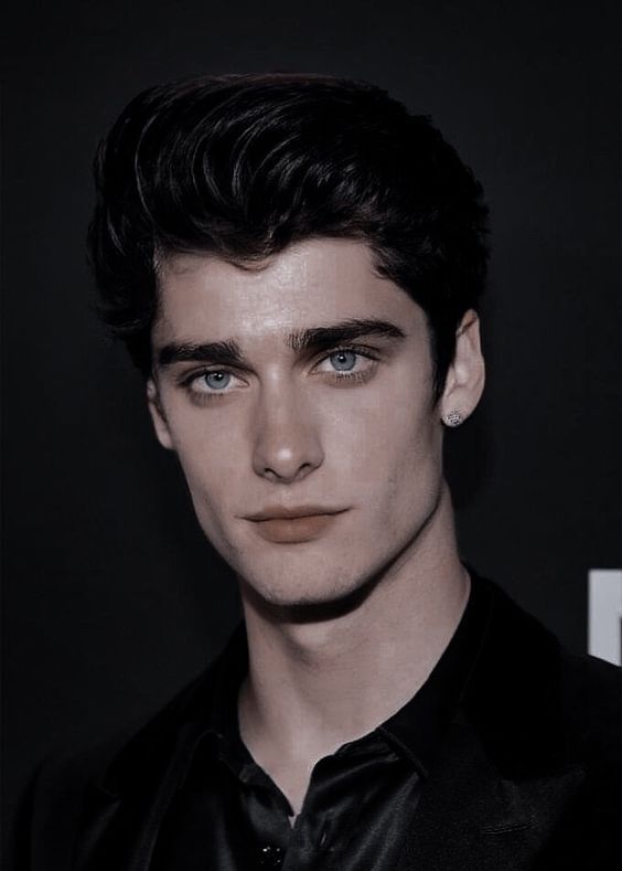 a close up of a person wearing a black shirt and tie with blue eyes looking at the camera