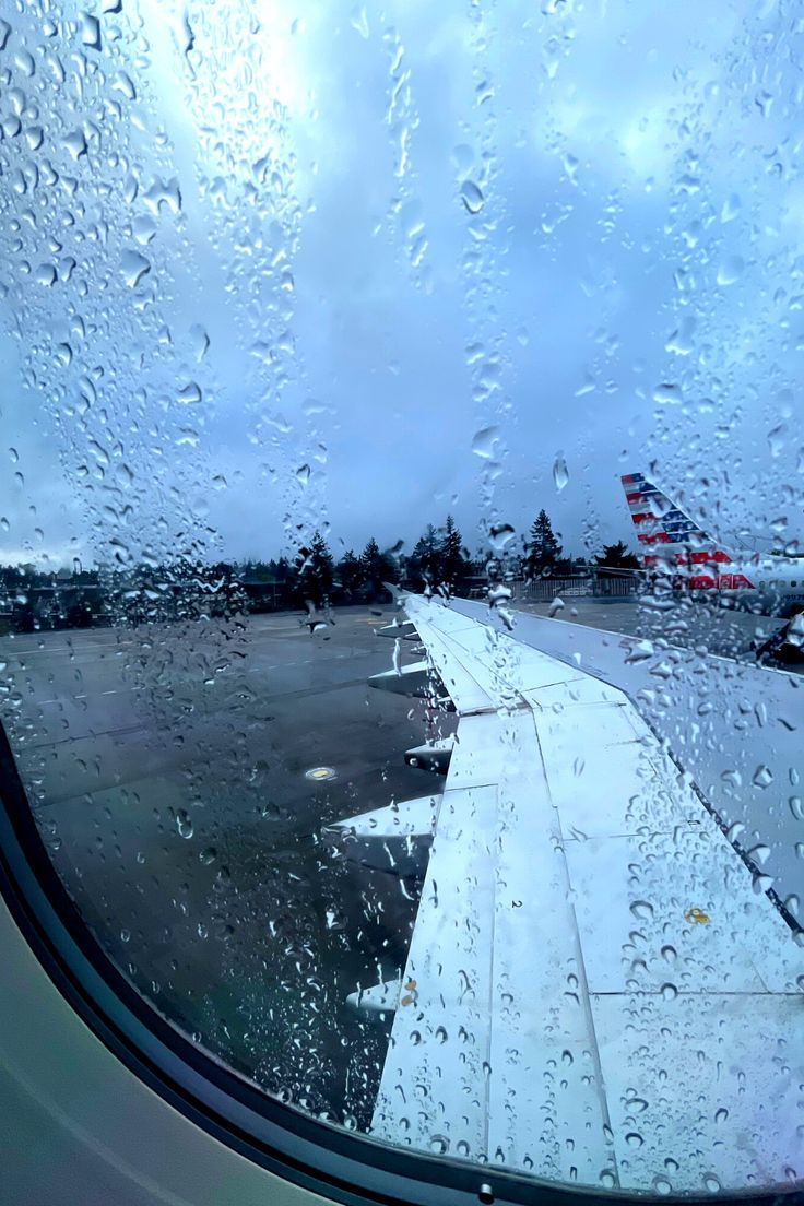 an airplane window with rain drops on it and the tarmac in the foreground