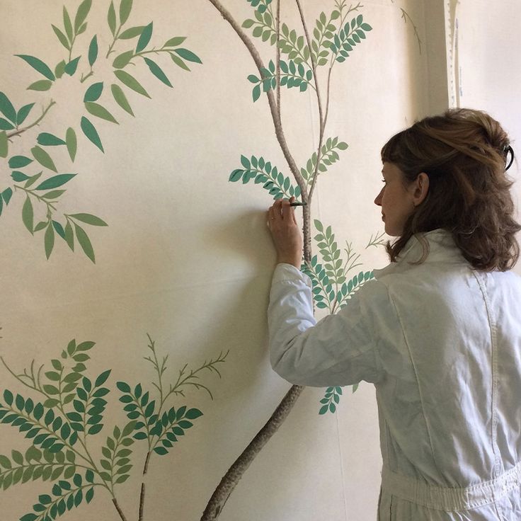 a woman painting a tree on the wall with green leaves and branches painted on it