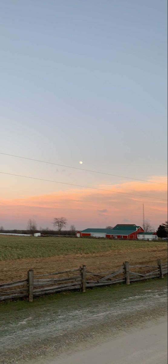 a field with a fence in the foreground and a red barn in the background