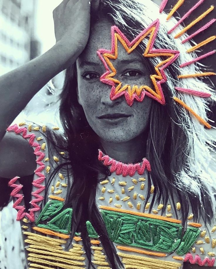 a woman with painted face and headdress holding her hands up to her forehead