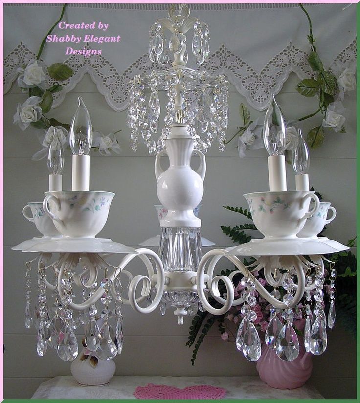 two white chandeliers sitting next to each other on top of a table with flowers in the background