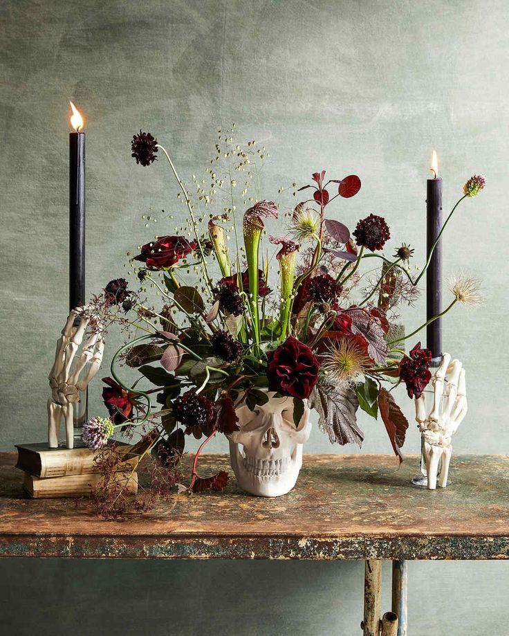 a table topped with a skull vase filled with flowers and two candles next to it