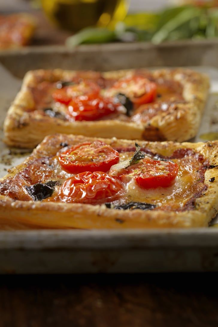 two square pizzas with tomatoes on them sitting on a table next to other food items